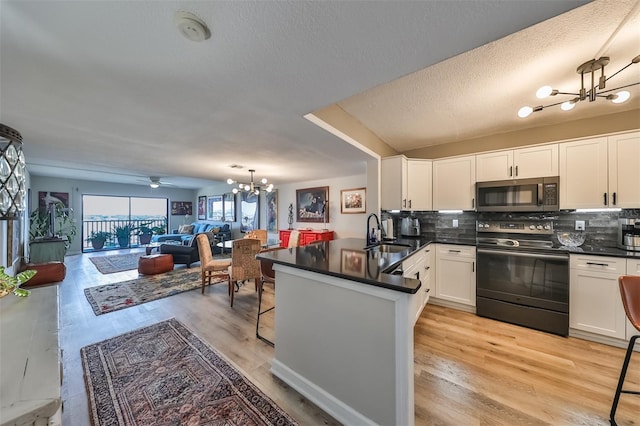 kitchen with tasteful backsplash, black / electric stove, kitchen peninsula, decorative light fixtures, and white cabinets