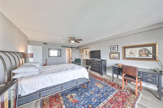 bedroom with a textured ceiling, light hardwood / wood-style flooring, and ceiling fan