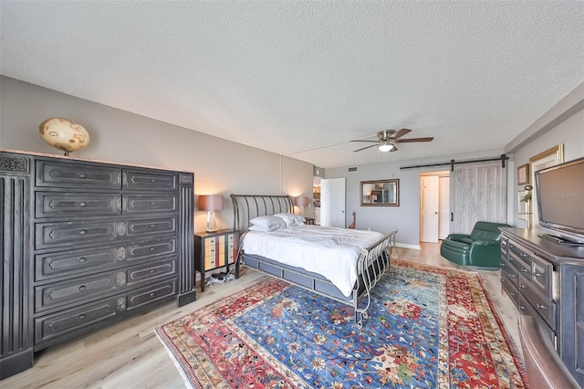 bedroom with ceiling fan, a barn door, a textured ceiling, and light hardwood / wood-style flooring