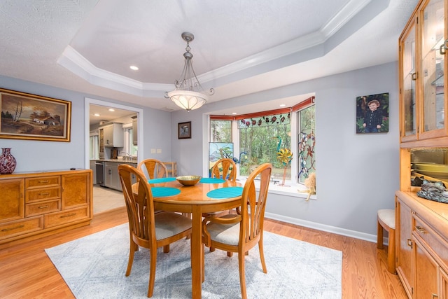 dining space with ornamental molding, sink, light wood-type flooring, and a tray ceiling