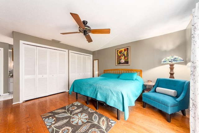 bedroom featuring wood-type flooring, two closets, and ceiling fan