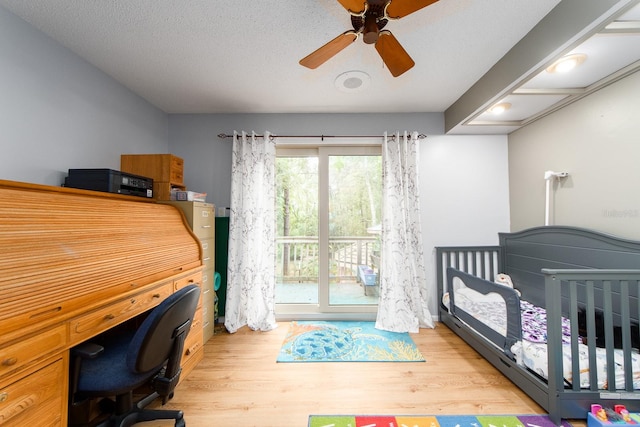 bedroom featuring ceiling fan, a textured ceiling, light hardwood / wood-style flooring, and a crib