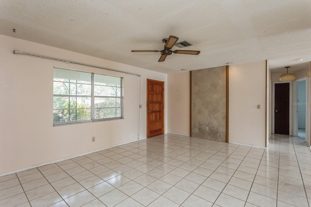 empty room featuring light tile patterned floors, a ceiling fan, visible vents, and a textured ceiling