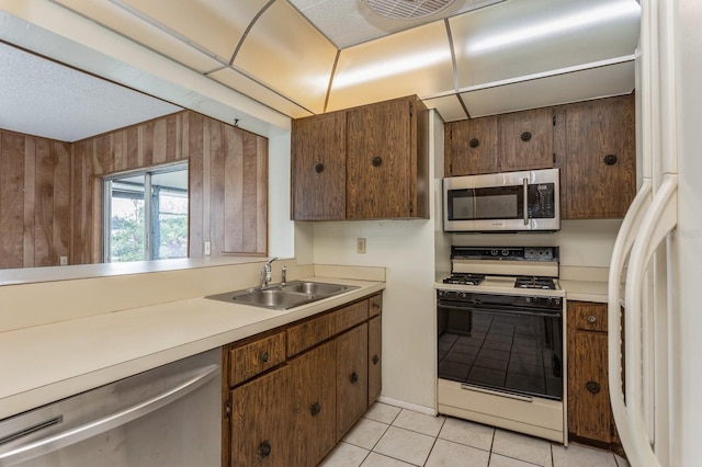 kitchen featuring light tile patterned flooring, a sink, stainless steel appliances, light countertops, and wood walls