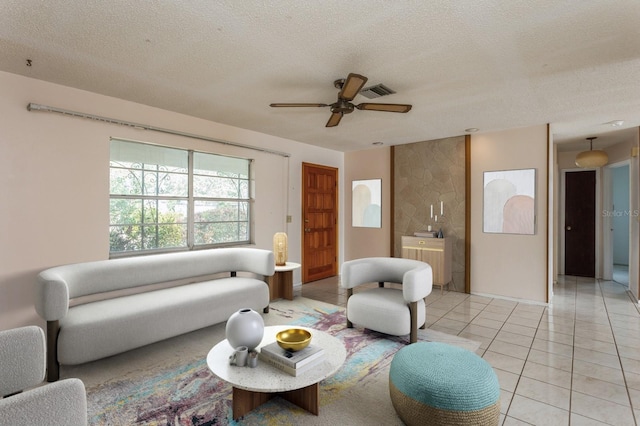 living room featuring light tile patterned floors, visible vents, a textured ceiling, and ceiling fan