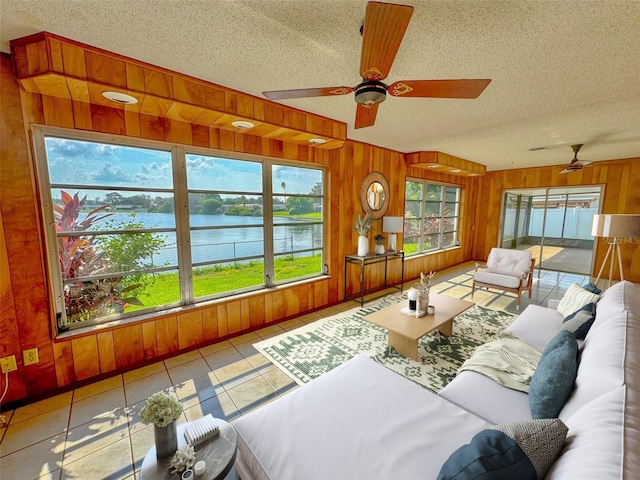 tiled living room with ceiling fan, a water view, a textured ceiling, and wood walls