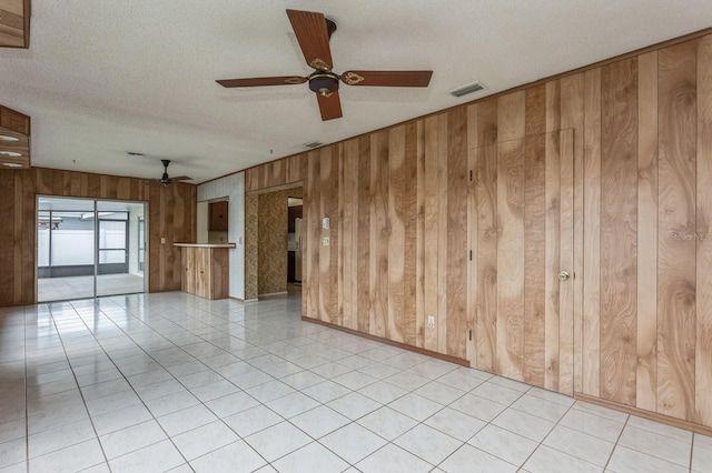 unfurnished room featuring light tile patterned floors, visible vents, wood walls, and a textured ceiling