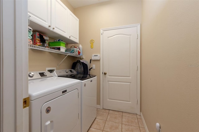 clothes washing area with cabinets, washer and dryer, and light tile patterned floors