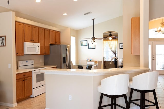 kitchen featuring white appliances, light tile patterned floors, kitchen peninsula, ceiling fan with notable chandelier, and a kitchen bar