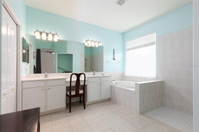 bathroom featuring tiled bath, a healthy amount of sunlight, tile patterned flooring, and dual bowl vanity