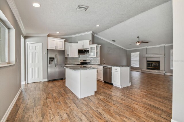 kitchen featuring crown molding, white cabinets, stainless steel appliances, hardwood / wood-style floors, and vaulted ceiling