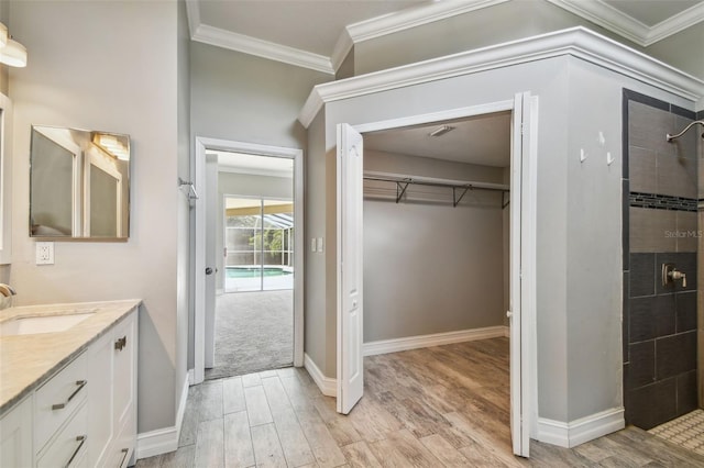 bathroom with hardwood / wood-style flooring, crown molding, vanity, and a tile shower