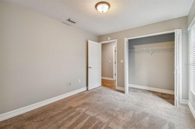 unfurnished bedroom with light carpet, a closet, and a textured ceiling