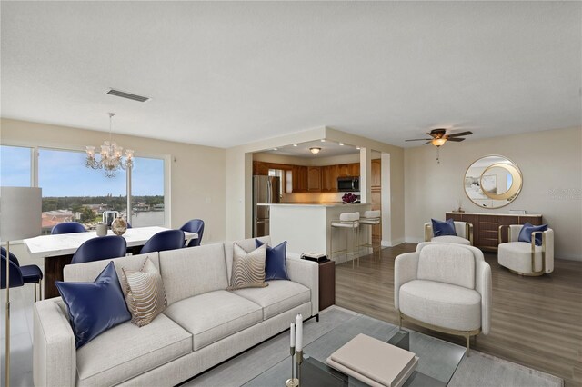 living room with visible vents, ceiling fan with notable chandelier, baseboards, and light wood-style floors