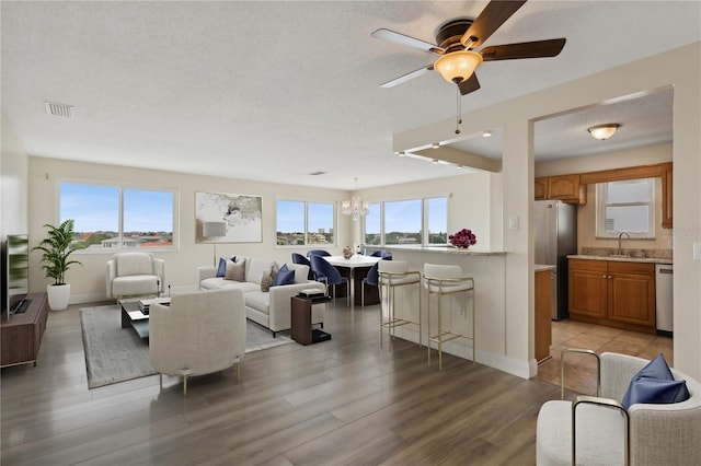 living room with sink, a textured ceiling, light hardwood / wood-style flooring, and ceiling fan with notable chandelier