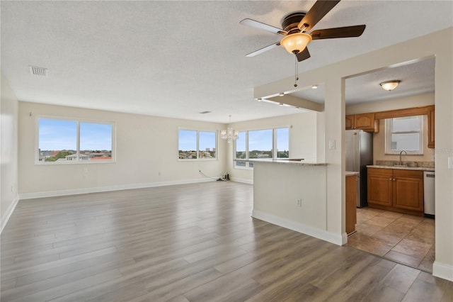 unfurnished living room with sink, a textured ceiling, light hardwood / wood-style flooring, and ceiling fan with notable chandelier