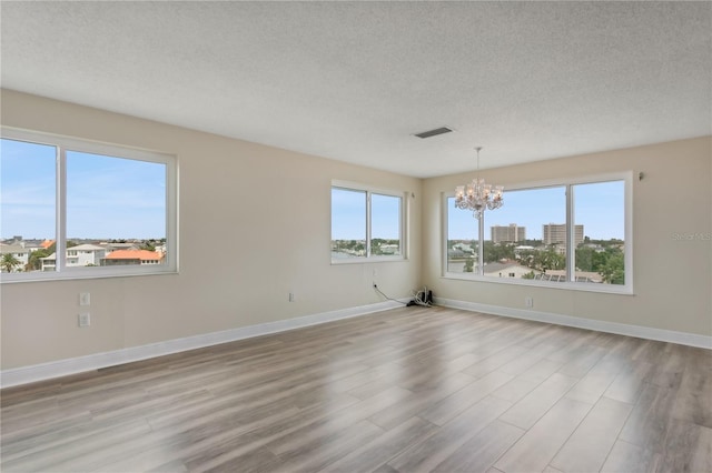 spare room featuring a textured ceiling, light hardwood / wood-style floors, and a chandelier