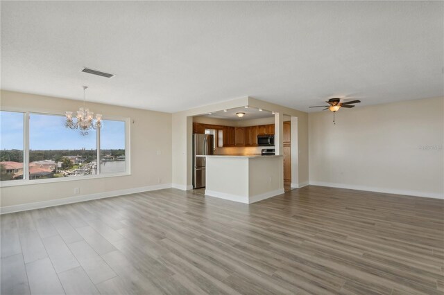 unfurnished living room with ceiling fan with notable chandelier and wood-type flooring