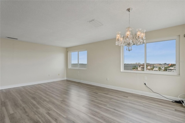 spare room with a textured ceiling, a notable chandelier, and hardwood / wood-style floors