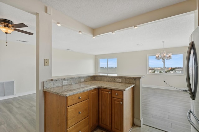 kitchen with light hardwood / wood-style flooring, light stone countertops, ceiling fan with notable chandelier, a textured ceiling, and kitchen peninsula