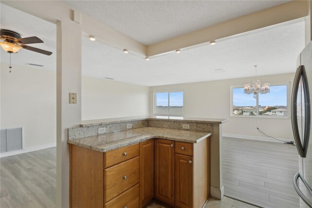 kitchen with visible vents, freestanding refrigerator, brown cabinetry, light stone countertops, and a healthy amount of sunlight