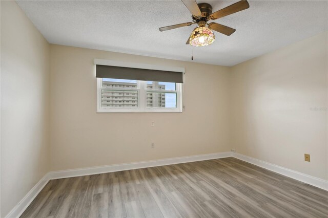 empty room with a textured ceiling, baseboards, and wood finished floors