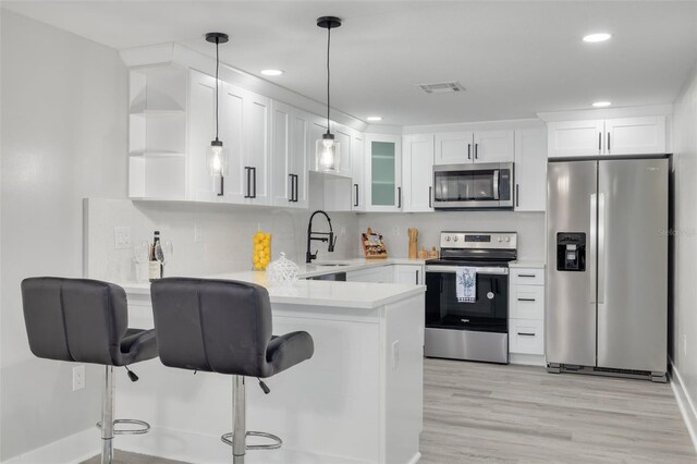 kitchen with kitchen peninsula, light hardwood / wood-style flooring, white cabinetry, stainless steel appliances, and a breakfast bar area