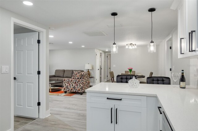 kitchen with light wood-type flooring, white cabinetry, kitchen peninsula, and hanging light fixtures