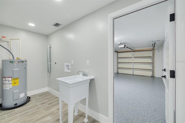 clothes washing area with light hardwood / wood-style flooring, water heater, electric dryer hookup, and hookup for a washing machine