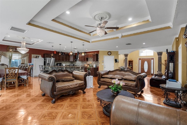 living room featuring a raised ceiling, crown molding, decorative columns, and ceiling fan