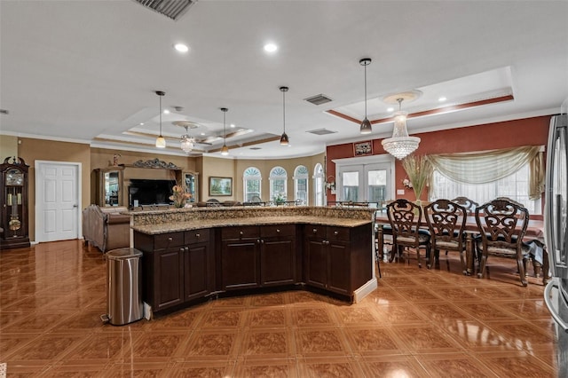 kitchen with hanging light fixtures, light stone counters, dark brown cabinetry, and a tray ceiling