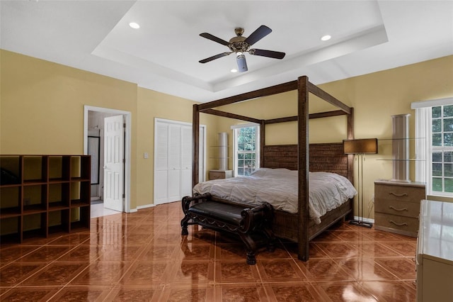 bedroom with ceiling fan, multiple windows, and a tray ceiling