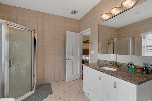 bathroom with a shower with shower door, vanity, tile walls, and tile patterned flooring