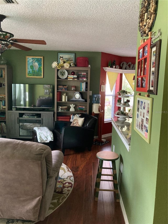 living room featuring ceiling fan, dark wood-type flooring, and a textured ceiling