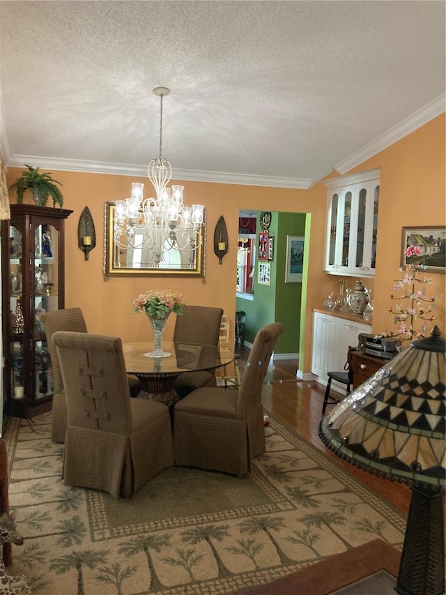 dining space with a textured ceiling, a notable chandelier, ornamental molding, and hardwood / wood-style floors