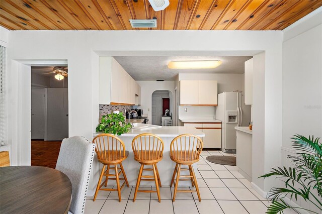 kitchen featuring backsplash, white refrigerator with ice dispenser, white cabinets, wooden ceiling, and kitchen peninsula