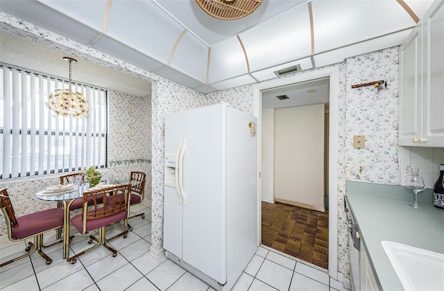 kitchen featuring light tile patterned floors, decorative light fixtures, a chandelier, white refrigerator with ice dispenser, and white cabinets