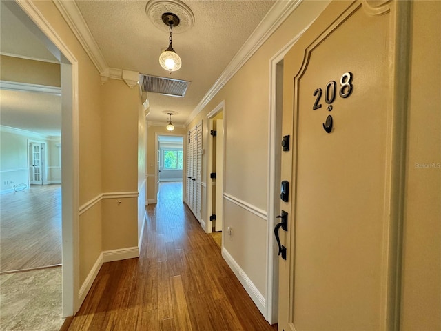 hall with hardwood / wood-style flooring, a textured ceiling, and ornamental molding