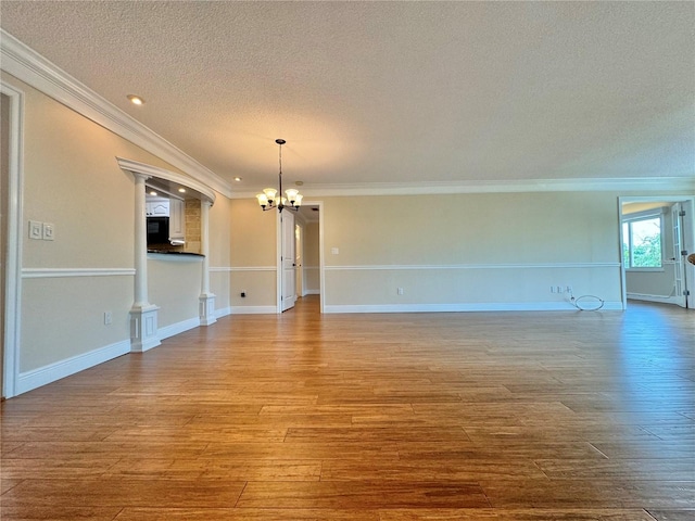 unfurnished living room with wood-type flooring, a notable chandelier, a textured ceiling, and ornamental molding