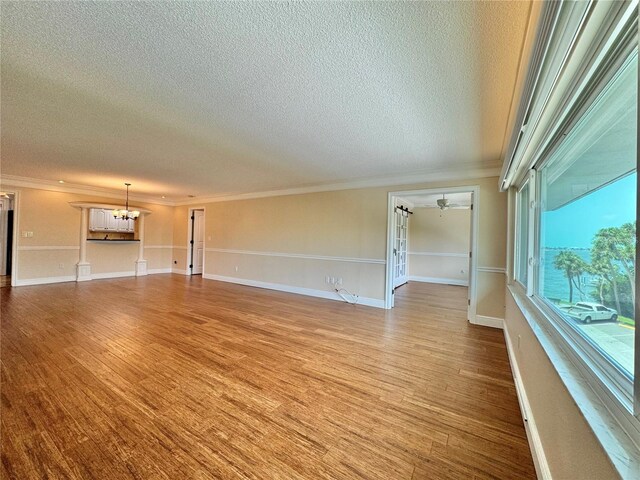 unfurnished living room with a textured ceiling, light hardwood / wood-style floors, ceiling fan with notable chandelier, and ornamental molding