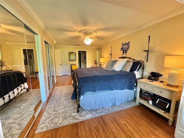 bedroom with hardwood / wood-style floors, multiple closets, crown molding, and ceiling fan