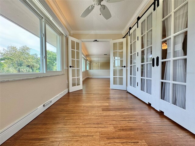 spare room featuring ornamental molding, french doors, wood-type flooring, a barn door, and ceiling fan