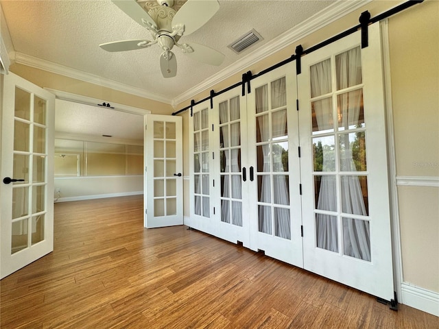 interior space featuring ceiling fan, wood-type flooring, french doors, and a barn door