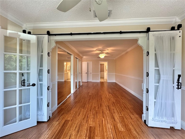 unfurnished room featuring hardwood / wood-style floors, a textured ceiling, ceiling fan, a barn door, and crown molding