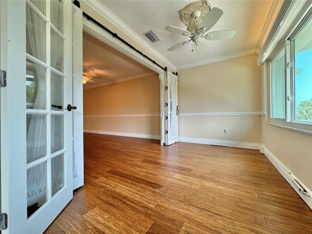 empty room with ceiling fan, crown molding, hardwood / wood-style flooring, and a barn door