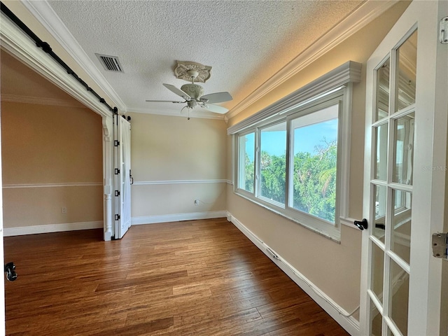 spare room featuring ceiling fan, crown molding, hardwood / wood-style flooring, and a barn door