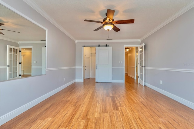 empty room with ceiling fan, ornamental molding, light wood-type flooring, and a barn door