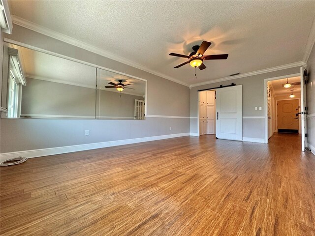 interior space with ceiling fan, light hardwood / wood-style flooring, a barn door, ornamental molding, and a textured ceiling