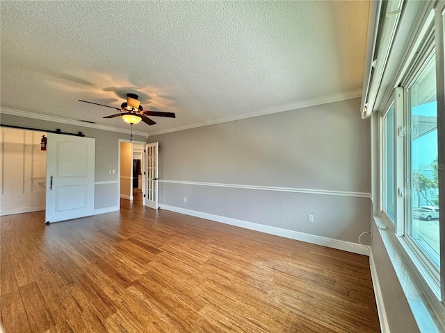 unfurnished room with ceiling fan, hardwood / wood-style floors, a barn door, a textured ceiling, and crown molding