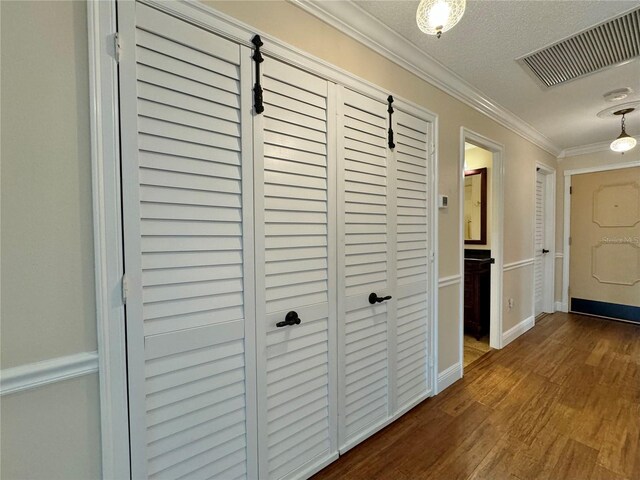 corridor featuring a textured ceiling, crown molding, and wood-type flooring